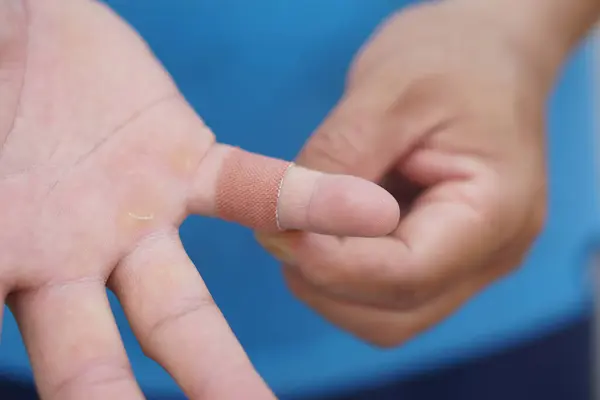 Close up man uses adhesive bandage tape to cover wound on finger. Concept, first aid. Self care for injury, to protect and prevent from dirt or germs into wound by covering adhesive bandage plaster.