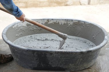 Çimento tozu, kum ve betonu karıştırmak için leğende taş karıştırmak için çapa kullanan yakın bir işçi. Kavram. İnşaat işçiliği. Çalışkandır. Çimentoyla yapılan inşaat süreci  