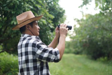 Asyalı botanikçi ormanda doğayı keşfetmek için dürbün tutuyor. Kavram, doğa keşfi. Araştırma, botanik bitkilerini araştırmak. Orman ve çevre koruma.   