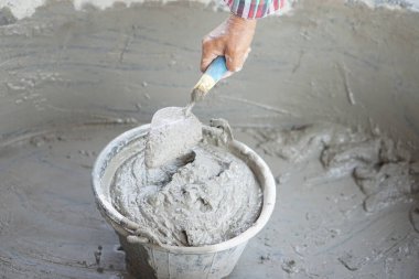 İşçi eli kapalı, kovaya ıslak çimento karıştırmak için bir mala tutunun. Kavram. İnşaat işi. İnşaat süreci çimentoyla işliyor. İnşa etmek için iyi kalite ve uygun malzeme ürünü seçin  