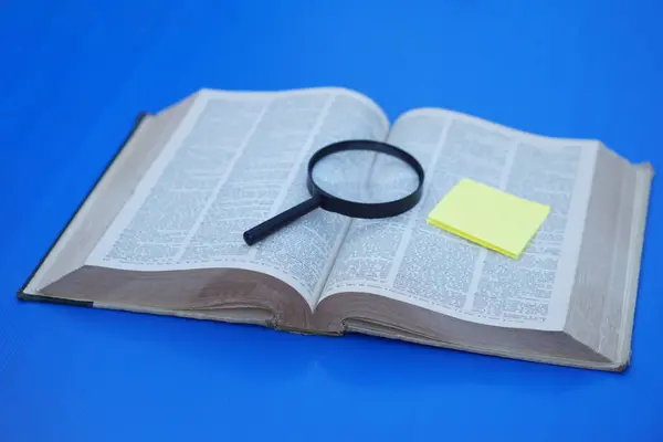 Büyüteç, sarı kağıt ve kitap. Konsept, eğitim. Kitap okuyarak cevap ya da bilgi topluyorum. Çalış ve araştır. Soruşturmaya dayalı öğrenme stratejisi. Okuma kitaplarından keşif.