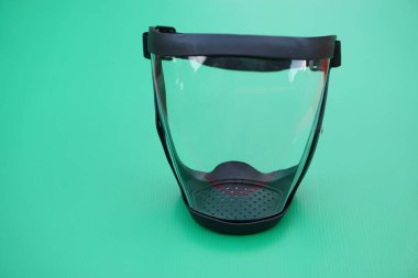 Koruyucu yüz kalkanı, siyah kenarlı temiz cam. Yeşil arka plan. Kavram, araç gereç, yüzü tozdan, mikroplardan ya da diğer yüzlerden korumak için kullanılan ekipman. İş Güvenli.