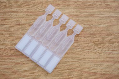 Tek kullanımlık yapay göz yaşartıcı göz damlası kapları, tüpler, kahverengi arka planda izole edilmiş. Kuru göz veya göz hastalığı tedavisi için tıbbi ürünler.    