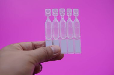 Tek kullanımlık yapay göz yaşartıcı göz damlası kapları, tüpler, pembe arka planda izole edilmiş. Kuru göz veya göz hastalığı tedavisi için tıbbi ürünler.    