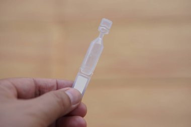 Tek kullanımlık yapay göz yaşartıcı göz damlası konteynırı, tüp, kahverengi arka planda izole edilmiş. Kuru göz veya göz hastalığı tedavisi için tıbbi ürünler.    