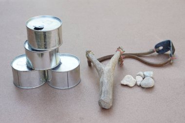 Sapan, eski kutular ve küçük kaya mermileri. Teneke atış oyunu için malzemeler. Kavram, geleneksel oyun, meydan okuma, taş kurşunla kutuları hedef al ve ateş et..                