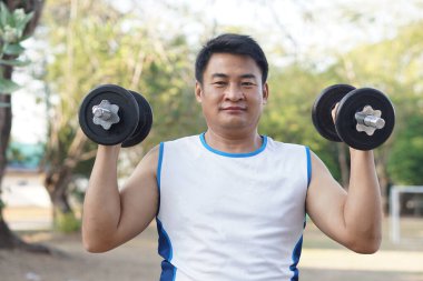 Yakışıklı Asyalı adam dışarıda egzersiz yapıyor, dambılı kaldırıyor. Konsept, vücut geliştirme egzersizi. Kaslarını güçlendir. Ağırlık kaldırma. Sağlıklı bir yaşam tarzı. Spor malzemeleri. Vücut çalışınca güçlenir..   
