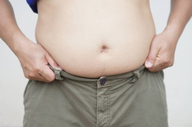 Yakından bakınca, koca göbekli olduğu için pantolonunu indirmeye çalışıyor. Kavram, şişman, aşırı kilolu, sağlık sorunu obezite, aşırı kilolu erkekler hastalıklara yol açabilir.            