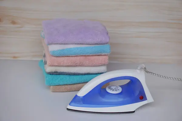 Electric iron and stack of folded clothes and on table. Concept, daily chore, household. ironing and folded clothes for neat and clean. Maintenance and keep garments.
