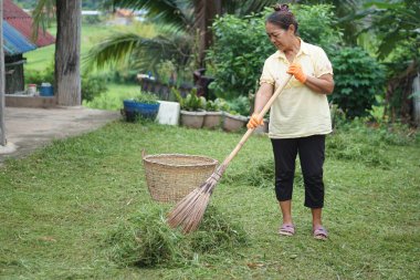 Asyalı kadın çimleri biçtikten sonra süpürmek için süpürge tutuyor. Evdeki ya da mahalledeki temizlik alanı kavramını. Ev işleri, boş zaman aktiviteleri. İyi çevre için toplum hizmeti, zararlı böceklerden korunma.
