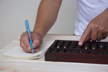 Close up man hand holds pen, write on paper and calculate on wooden abacus. Concept, ancient style calculation. Counting equipment. Calculator. Educational material.              clipart