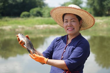 Mutlu Asyalı orta yaşlı kadın çiftçi şapka takar, gölette balık tutar. Tarım yaşam tarzı kavramı. Çiftçi iş olarak balık yetiştirir ya da ekmek ya da satmak için para kazanır.               