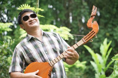 Yakışıklı Asyalı adam geleneksel Tayland gitarı çalıyor, folk gitar. Kavram, müzik, hobi, eğlence aktivitesi. Rahatlama zamanı. Müzik zihinsel sağlığı geliştirebilir.        