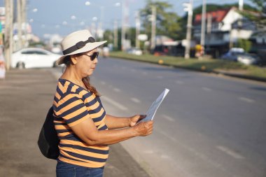 Asyalı kadın turist yaya yolunda duruyor, tek başına seyahat ederken haritaya bakıyor. Yaşlı kadın, emekli olduktan sonra seyahate çıkıyor. Konsept, seyahat yaşam tarzı.                                   