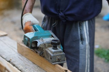 Marangoz, marangozluk alanında ahşap kalası olan elektrikli planör kullanıyor. Konsept, alet ya da inşaat malzemeleri. Güvenlik için dikkatli ve becerikli bir şekilde kullanın..       