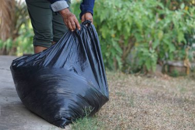 Kapalı el, içinde çöp olan siyah plastik torbayı tutuyor. Konsept, atık yönetimi. Çevre sorunları. Günlük ev işleri. Çöpleri at. Çöp tasnif etme.    