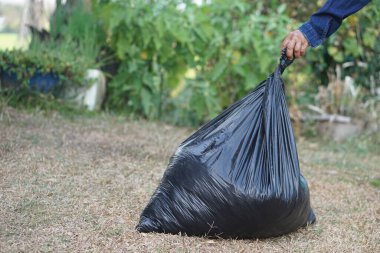 Kapalı el, içinde çöp olan siyah plastik torbayı tutuyor. Konsept, atık yönetimi. Çevre sorunları. Günlük ev işleri. Çöpleri at. Çöp tasnif etme.  