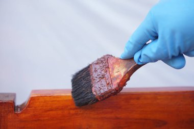 Kapalı el giyin mavi eldiven giy ahşap kalas üzerine boya yapmak için fırça tut. Mobilya kullanımı için konsept, yeniden boyama ve bakım. Yenileme, onarım ve ölüm hobisi.                                   