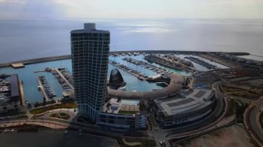 Ayia Napa Kıbrıs. Ayia Napa Marina 'nın kuş bakışı manzarası. Güneşli bir günde yüksek binalar ve marina. Akdeniz ve modern mimari. Denizin arka planına karşı doğa ve şehircilik.
