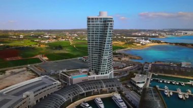 Ayia Napa Kıbrıs. Ayia Napa Marina 'nın kuş bakışı manzarası. Güneşli bir günde yüksek binalar ve marina. Akdeniz ve modern mimari. Denizin arka planına karşı doğa ve şehircilik.