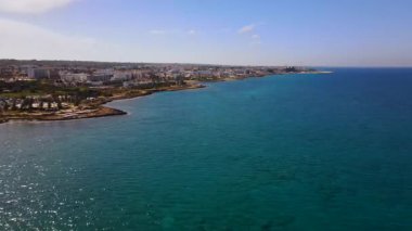 Protaras, Kıbrıs 'ta yaz günleri. Kamera turkuaz Akdeniz 'in ve otellerle çevrili sahil hattının üzerinden uçuyor..