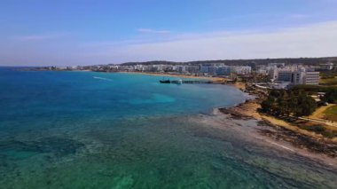 Protaras, Kıbrıs 'ta yaz günleri. Kamera turkuaz Akdeniz 'in ve otellerle çevrili sahil hattının üzerinden uçuyor..