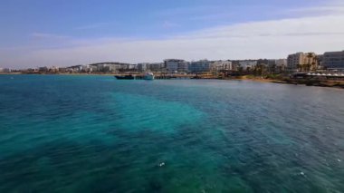 Protaras, Kıbrıs 'ta yaz günleri. Kamera turkuaz Akdeniz 'in ve otellerle çevrili sahil hattının üzerinden uçuyor..