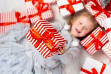 Selective focus. Focus on presents. Blurry happy funny child girl holding gift boxes lying on floor surrounded presents. Top view Little Kid fools around on Christmas morning. New years concept.