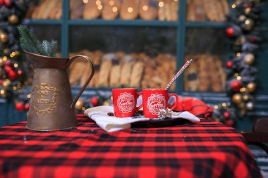 Two red cups of coffee on the table. Bakery exterior with Christmas decorations and fresh bread in showcase. Cozy outdoor bistro on Christmas eve. Copy space. christmas, seasonal greetings concepts