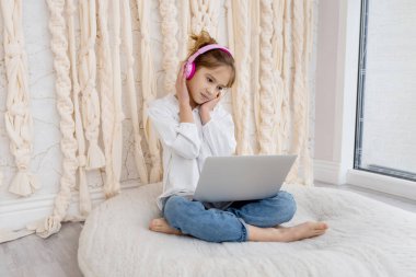 Portrait of caucasian girl in wireless headset using laptop, studying online at home. School pupil looking at pc screen, listening to music, watching online webinar, doing homework. Remote education