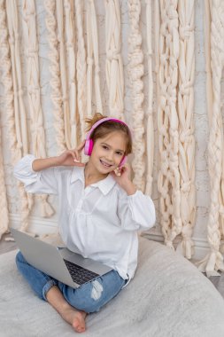 Happy caucasian girl listening to music, sitting on rug at homes. Smiling teenage relaxing, spend time with pink headphones and tablet at morning, Time to relax. People, leisure, technology concept
