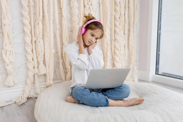 Portrait of caucasian girl in wireless headset using laptop, studying online at home. School pupil looking at pc screen, listening to music, watching online webinar, doing homework. Remote education