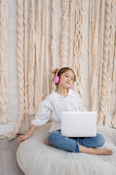 Happy caucasian girl in casual clothes, resting, listening to music in pink headphones. Good mood. Smiling peaceful carefree teeneger enjoying spending free time with favorite audio tracks. Hobby