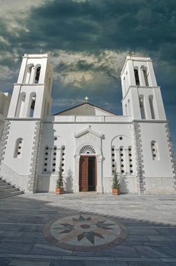 Beyaz Panagia Theoskepasti Ortodoks Kilisesi mavi detaylar ve Andros Adası 'ndaki çan kulesi dramatik bulutlu gökyüzü altında