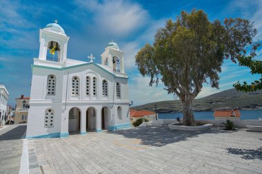 Mavi detayları ve Andros Adası 'ndaki çan kulesiyle dramatik bulutlu gökyüzü altında Beyaz Aziz George Ortodoks Kilisesi