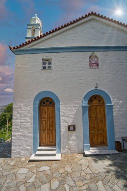 Andros Adası 'ndaki mavi detayları ve çan kulesiyle dramatik bulutlu gökyüzü altında Beyaz Rum Ortodoks Kilisesi