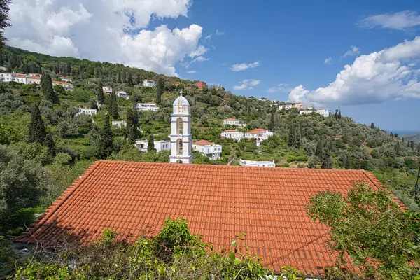 Andros Adası 'ndaki açık mavi gökyüzünün altında kırmızı kiremitli çatının arkasında haçlı beyaz çan kulesi.