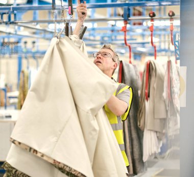 Kent, UK, 01.01.2024 dikiş makinesi işçileri tekstil fabrikasında çalışıyor. Metal silindirlerde metal pamuk askıları. Pamuk dikiş ve imalat tekstil endüstrisi. Metal askı rayları.