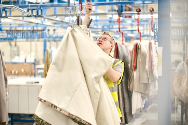 Kent, UK, 01.01.2024 dikiş makinesi işçileri tekstil fabrikasında çalışıyor. Metal silindirlerde metal pamuk askıları. Pamuk dikiş ve imalat tekstil endüstrisi. Metal askı rayları.