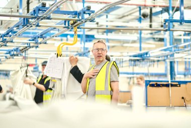 Kent, UK, 01.01.2024 dikiş makinesi işçileri tekstil fabrikasında çalışıyor. Metal silindirlerde metal pamuk askıları. Pamuk dikiş ve imalat tekstil endüstrisi. Metal askı rayları.