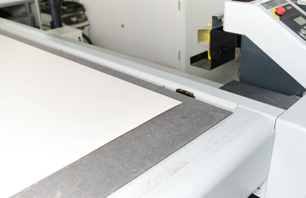 A laser cutting machine cutting out intricate design cardboard templates in a white clinical manufacture factory warehouse. Laser cutters in the industrial sector.