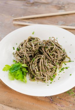 Organic brown noodles cooked in garlic oil, fresh coriander and sea salt. Served with chopsticks on a white plate.gourmet eating. clipart