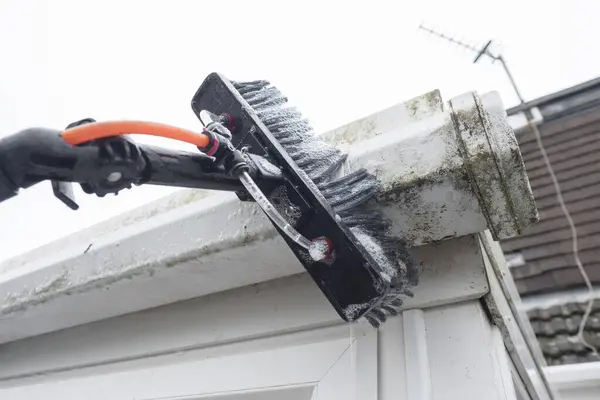 Kirli, tıkanmış, beyaz plastik pvc olukları temizleyen ve yosunlu yeşil plastik fasialarla boruları boşaltan bir fırça. Tıkanmış kanallar ve oluklar için pencere temizleyicileri ve iyi drenaj için düzenli bahçe bakımı gerekiyor.