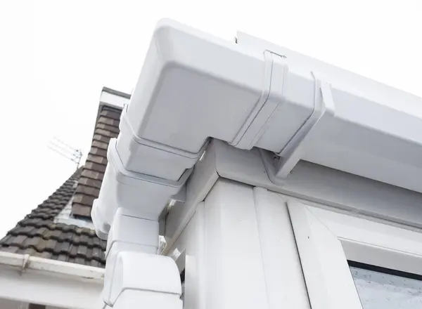 stock image Cleaned white plastic pvc gutters and drain pipes that were blocked and full of green mould on the plastic fascias.  Blocked drains and guttering need window cleaners and regular maintenance for good drainage.