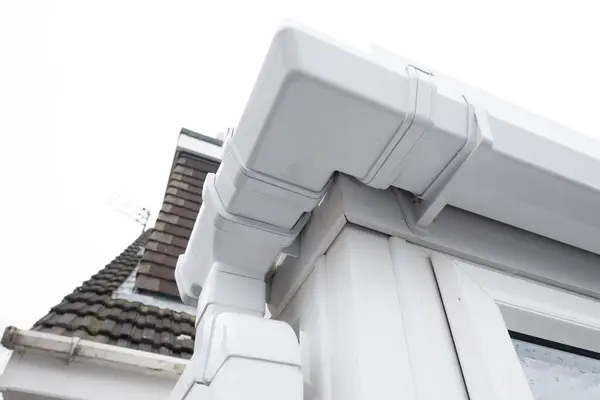 stock image Cleaned white plastic pvc gutters and drain pipes that were blocked and full of green mould on the plastic fascias.  Blocked drains and guttering need window cleaners and regular maintenance for good drainage.