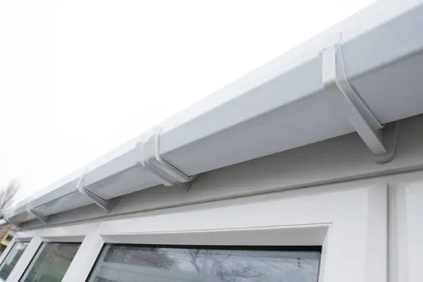 stock image Cleaned white plastic pvc gutters and drain pipes that were blocked and full of green mould on the plastic fascias.  Blocked drains and guttering need window cleaners and regular maintenance for good drainage.