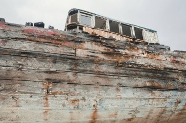 Çürüme ve bozulma belirtileri gösteren eski bir ahşap gemi enkazı. Paslı, çürümüş kalıntılarla kıyıda karaya vurmuş eski bir deniz gemisi. Doğa ve deniz eski teknelere zarar veriyor..