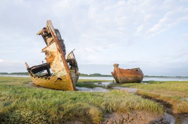 Çürüme ve bozulma belirtileri gösteren eski bir ahşap gemi enkazı. Paslı, çürümüş kalıntılarla kıyıda karaya vurmuş eski bir deniz gemisi. Doğa ve deniz eski teknelere zarar veriyor..