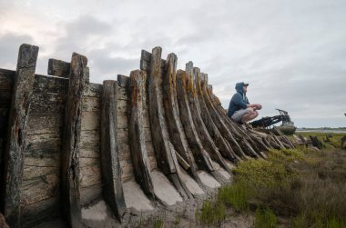 Çürüme ve bozulma belirtileri gösteren eski bir ahşap gemi enkazı. Paslı, çürümüş kalıntılarla kıyıda karaya vurmuş eski bir deniz gemisi. Doğa ve deniz eski teknelere zarar veriyor..