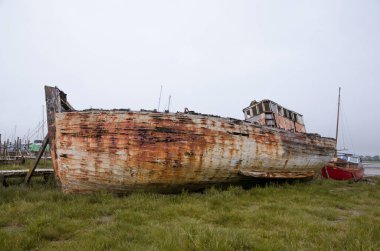 Çürüme ve bozulma belirtileri gösteren eski bir ahşap gemi enkazı. Paslı, çürümüş kalıntılarla kıyıda karaya vurmuş eski bir deniz gemisi. Doğa ve deniz eski teknelere zarar veriyor..